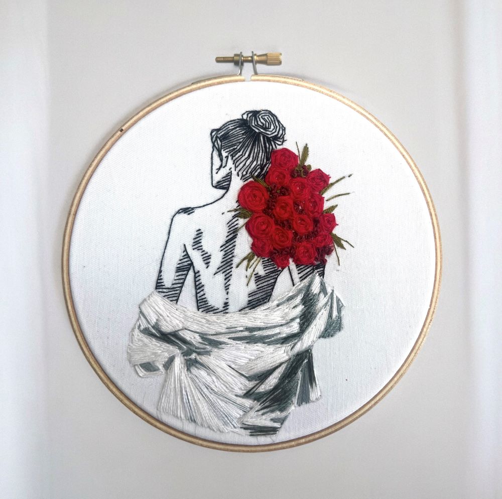 embroidery pattern including rose and fabric detail hung in bedroom
