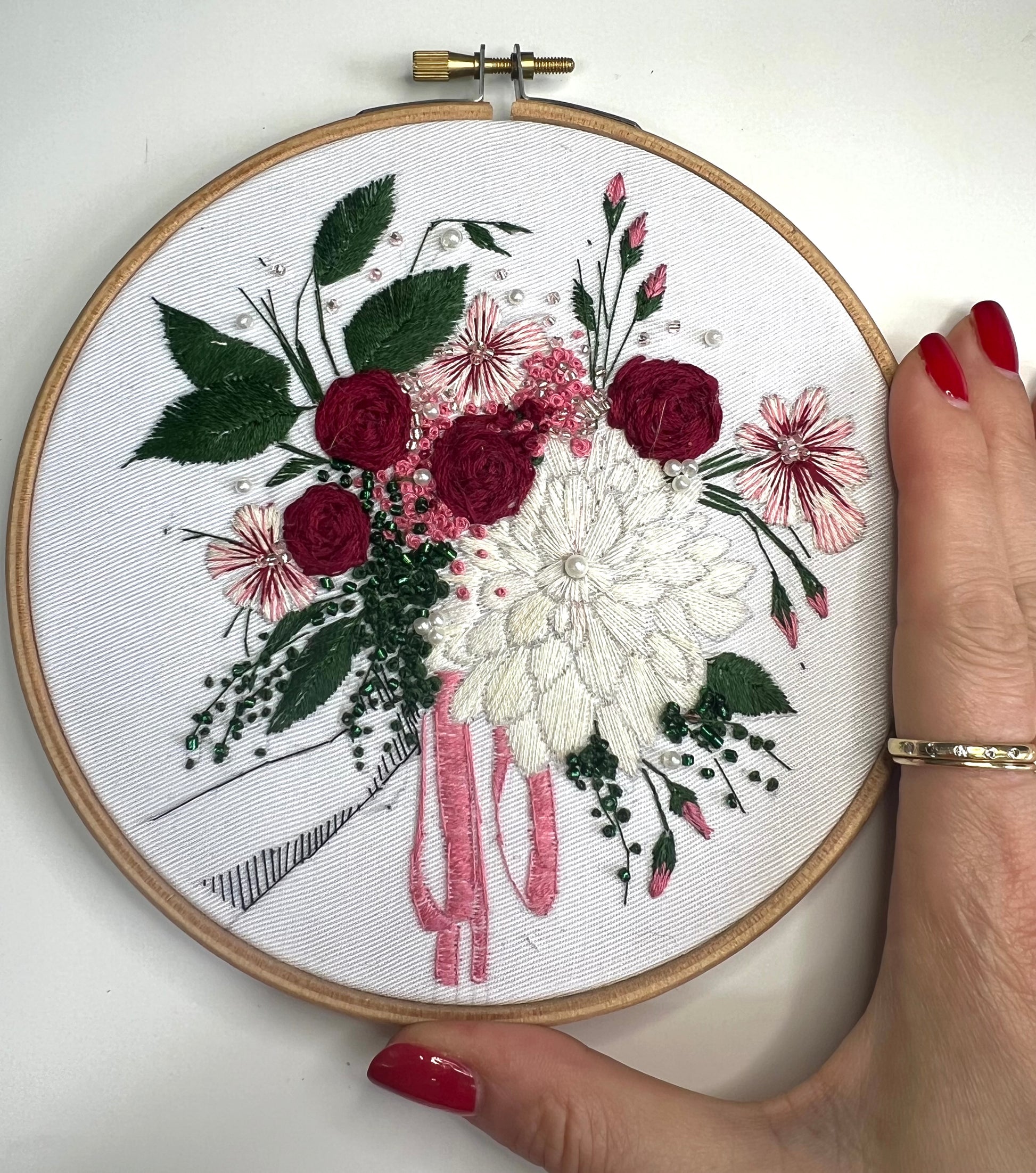 Red and green floral embroidery pattern with hand for scale